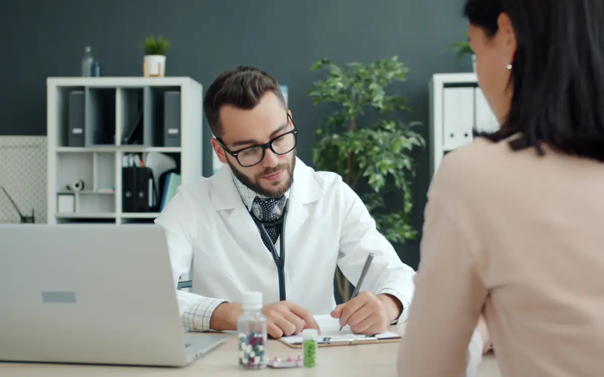 A doctor consulting a patient with a laptop on the desk
